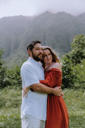 Couple in white shirt and red dress embrace in front of dramatic mountain landscape.