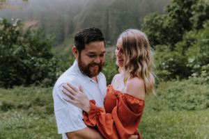 Romantic couple embraces in a lush mountain landscape with misty peaks in the background.