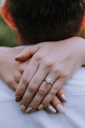Close-up of hands showing sparkly engagement ring and manicured nails.