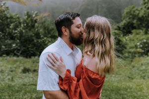 Couple shares an intimate moment against a backdrop of green mountains and misty skies.