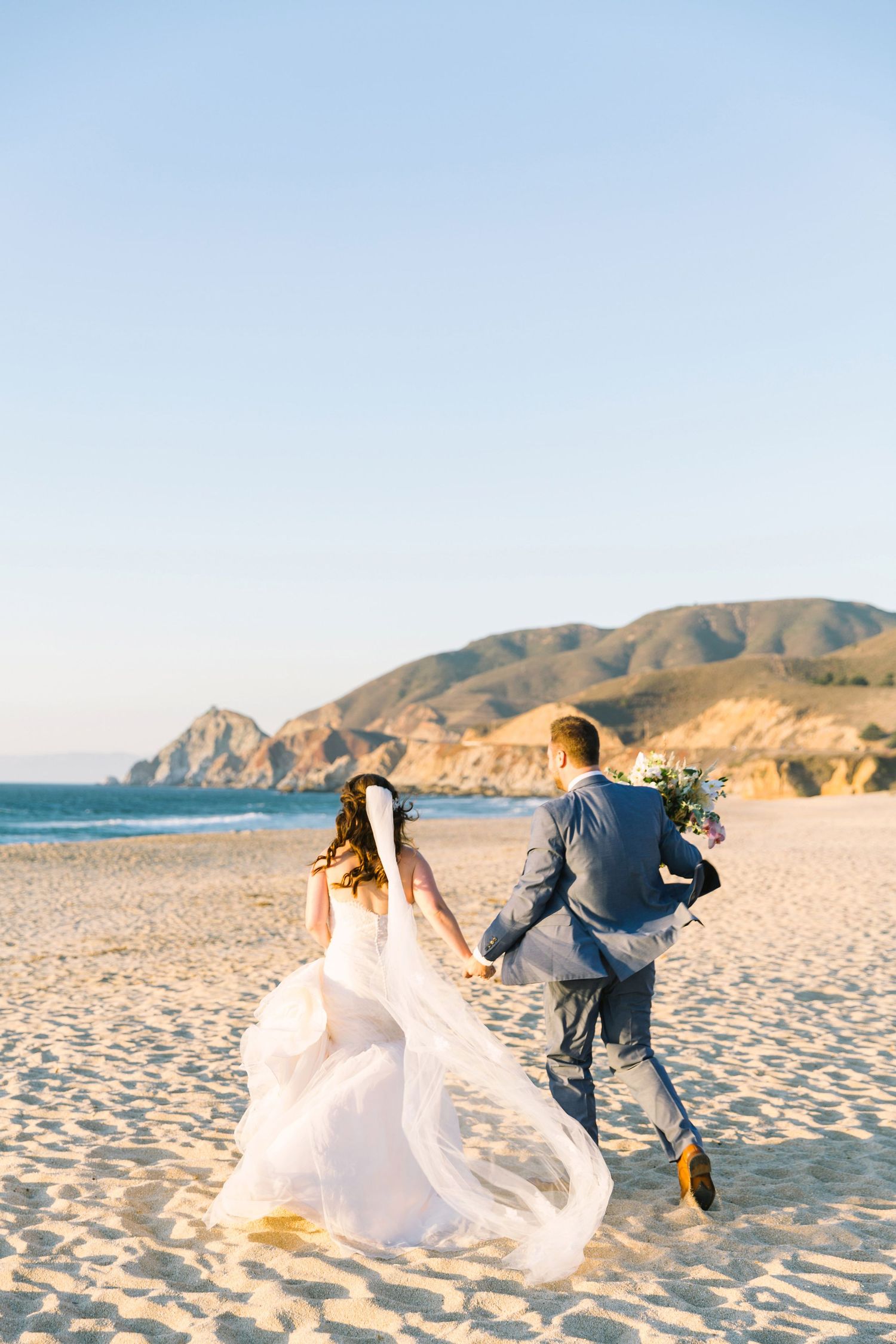 Married couple running on California beach at sunset