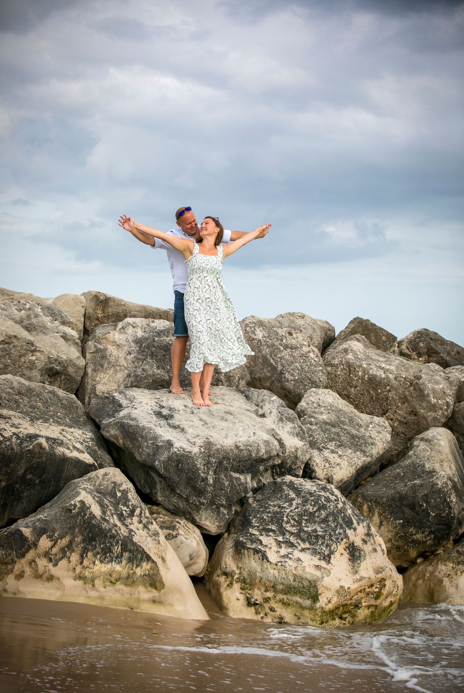 Two people enjoy a carefree moment on rocky coastal formations by the ocean.