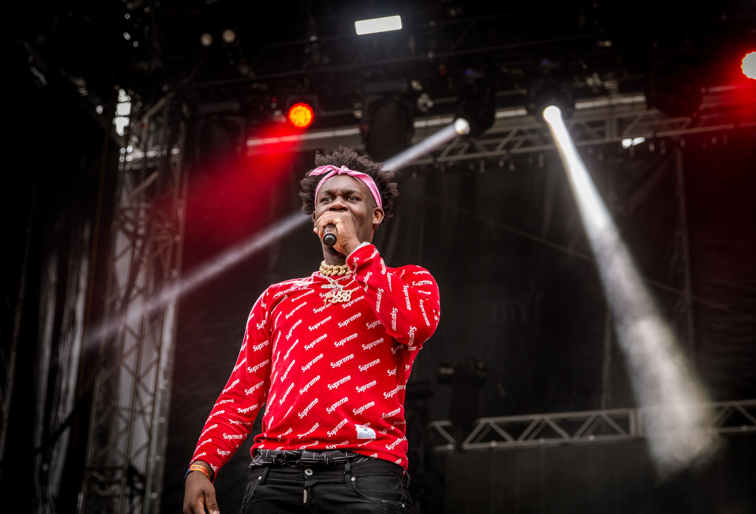 Performer in red shirt singing on stage with bright lights and smoke effects.