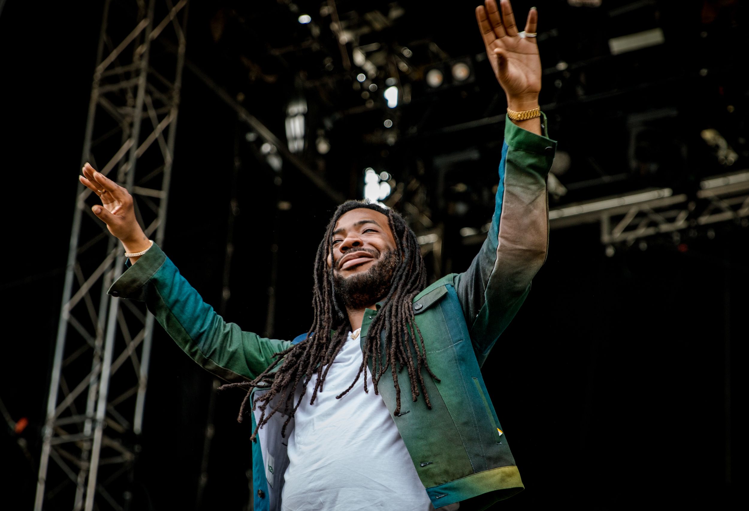 Performer in green jacket on stage with arms raised and joyful expression.