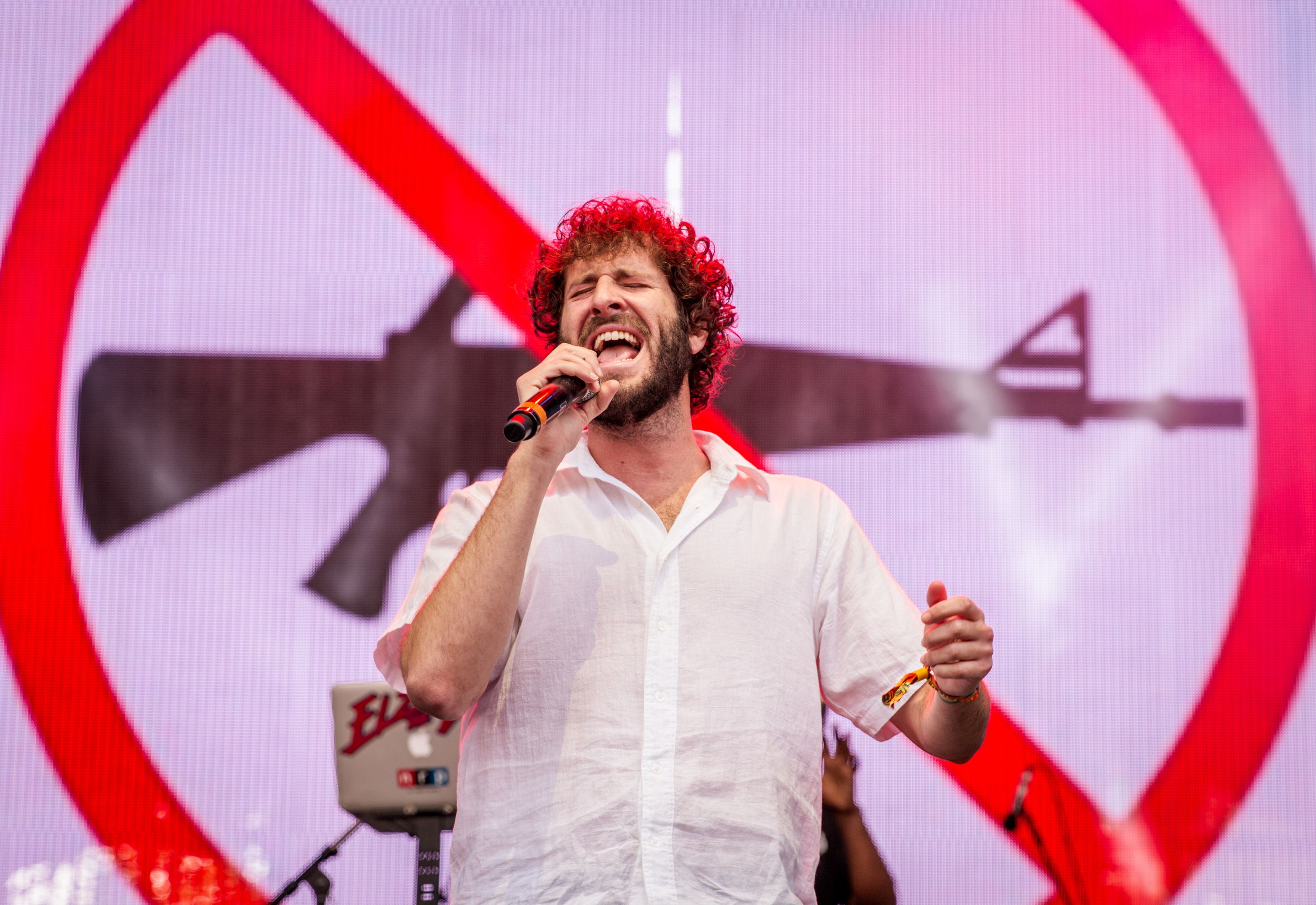 Singer in white shirt performing on stage with large no symbol backdrop.