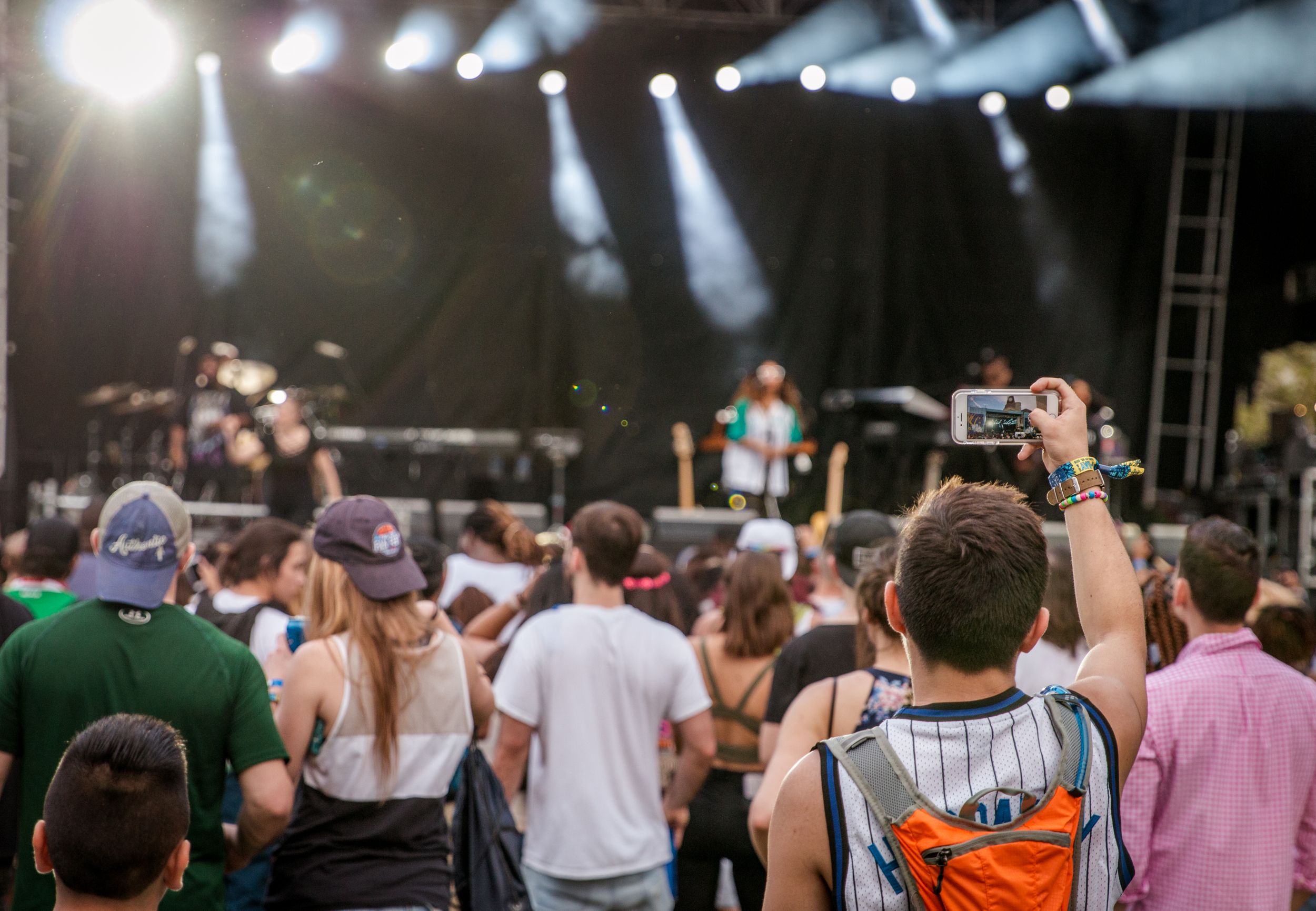 Concertgoers watching a performance with hands raised and smartphones recording at an outdoor music festival.