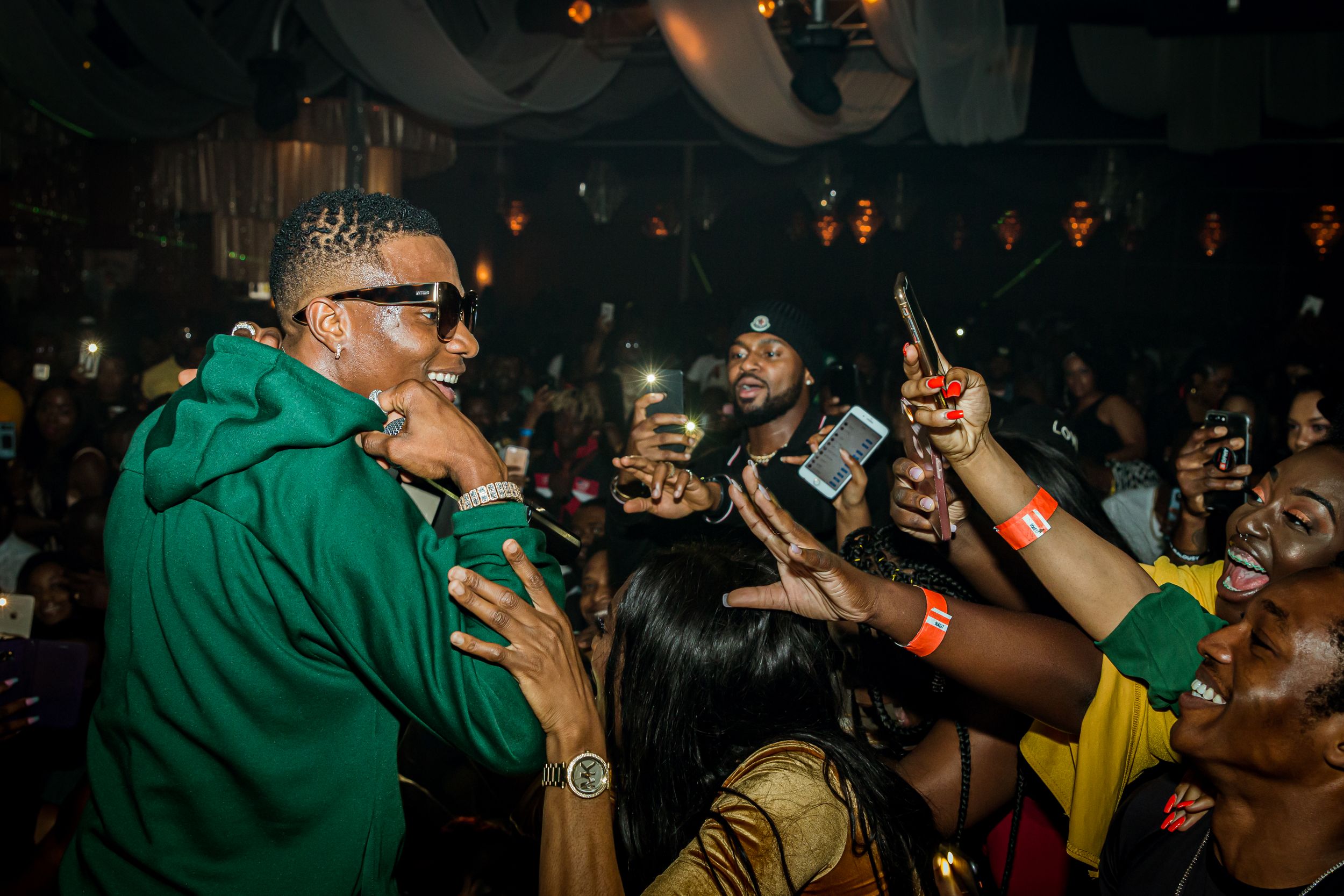 Performer in green jacket surrounded by enthusiastic fans in a crowded nightclub.