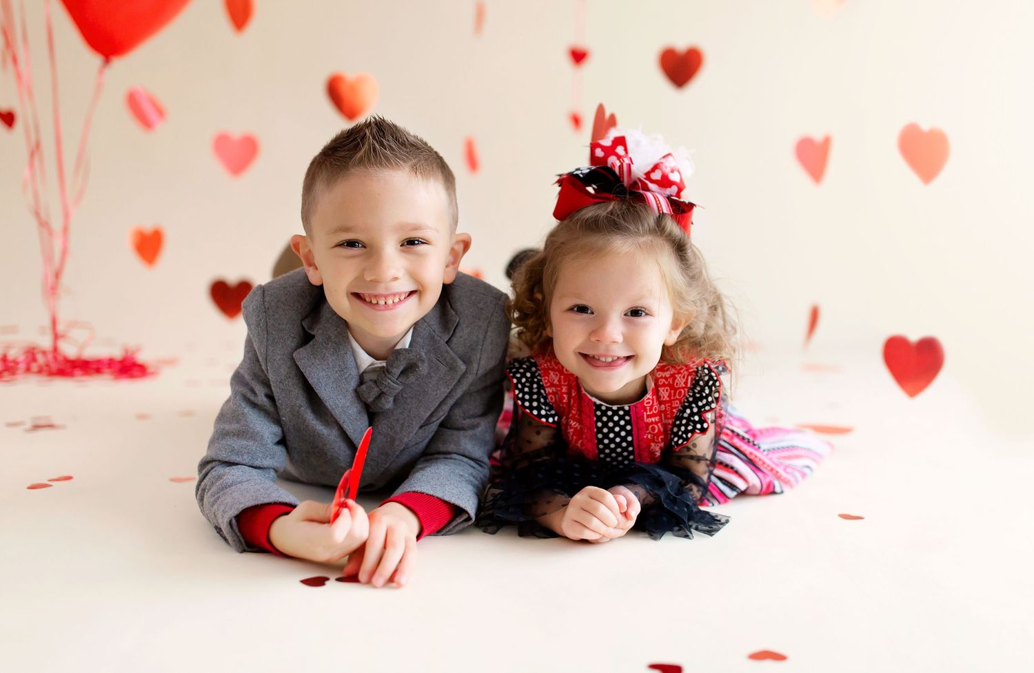 Two children lying on floor with red heart decorations for Valentine's Day themed photo.