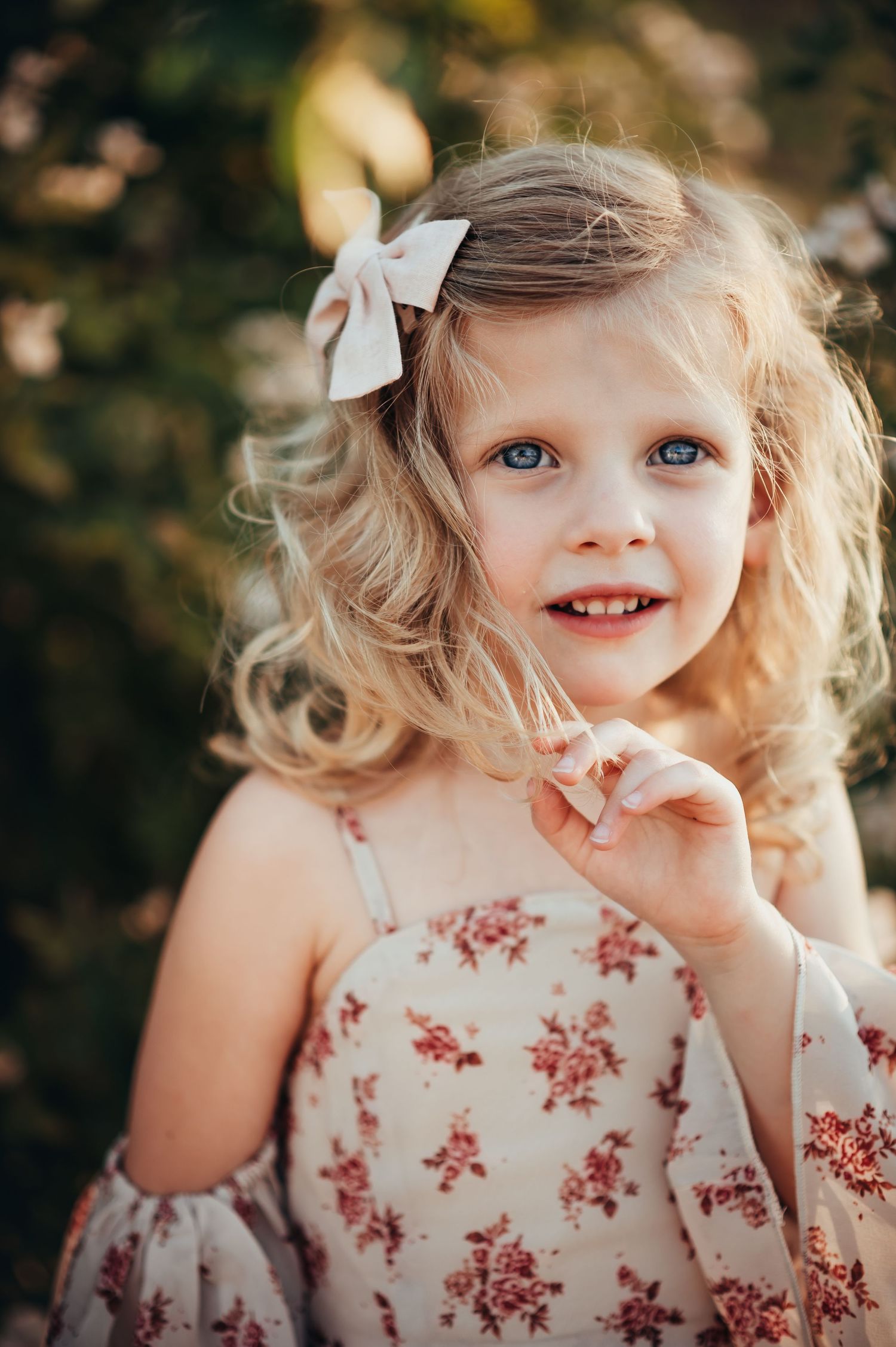 Little 4 year old girl with blue eyes looks sweetly at camera while holding her blonde curly hair for milestone photo