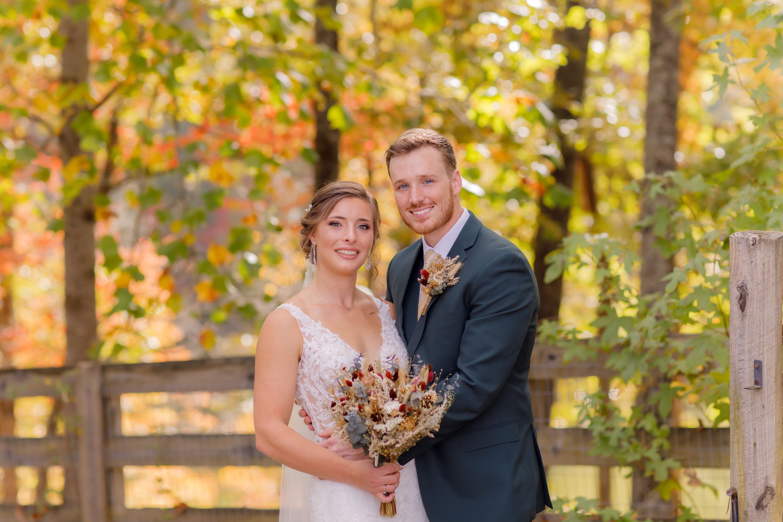 Newlyweds pose for a portrait with autumn foliage in the background.