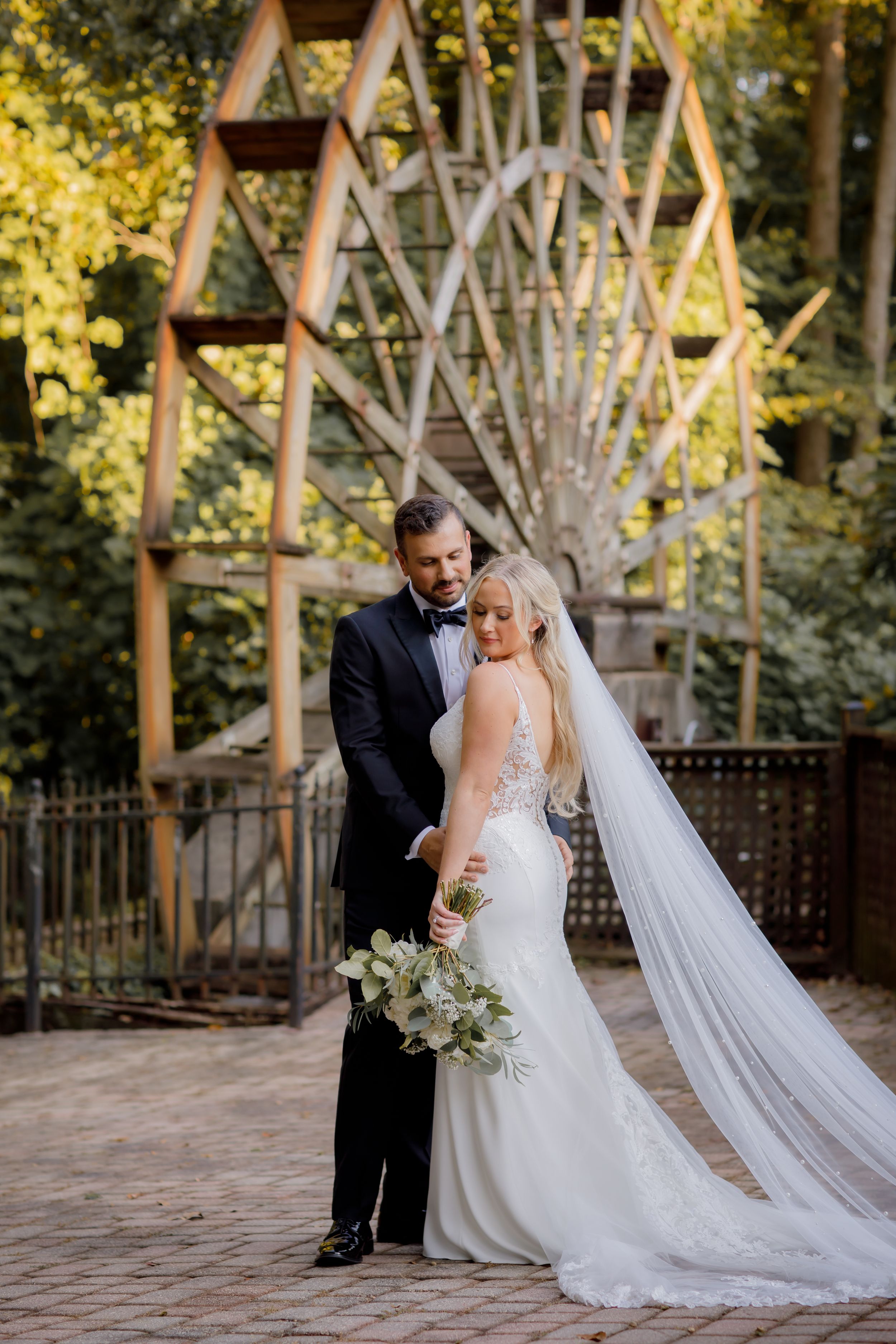 A bride and groom pose in front of a wooden Ferris wheel structure in a romantic outdoor setting.