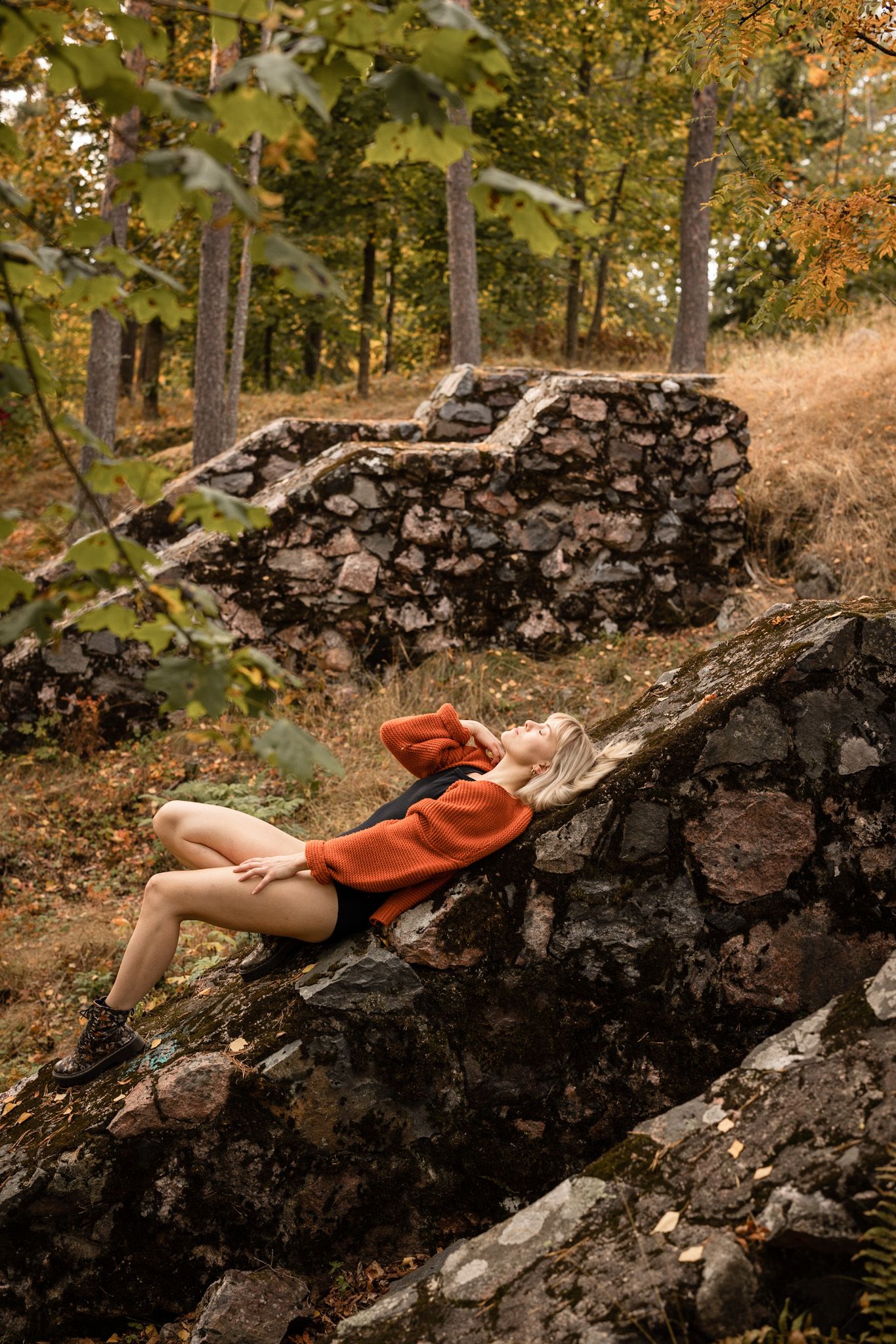 Woman laying on stone construction with her eyes closed, wearing only boots, cardigan and body.