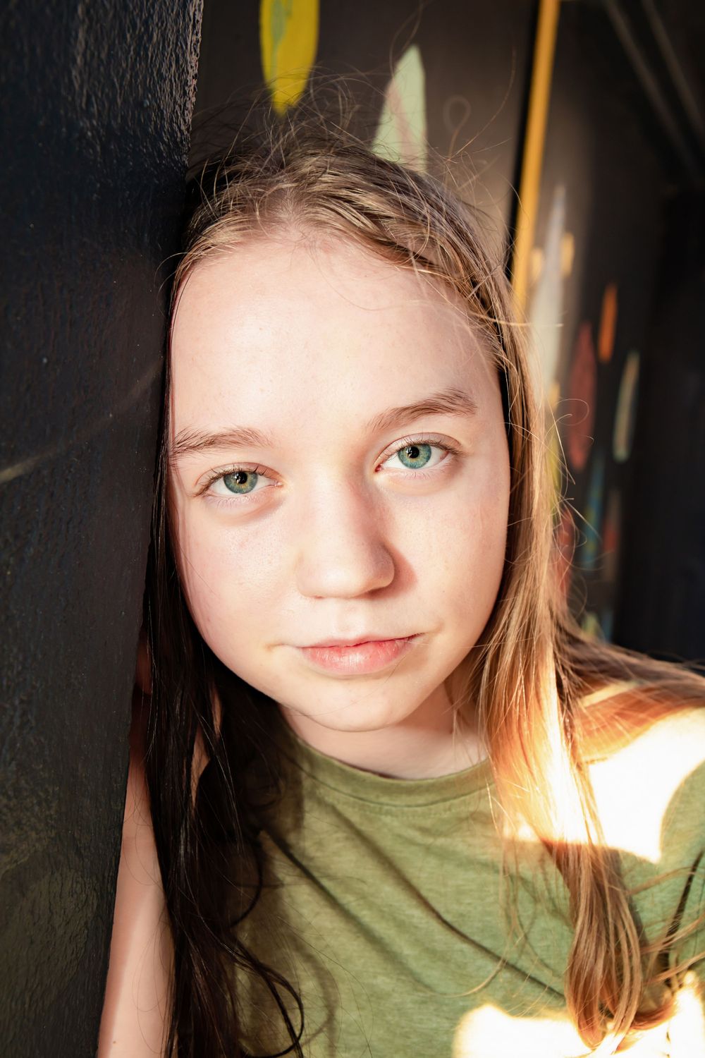 Portrait shot with dramatic lighting against a dark wall with light patterns creating shadow effects.