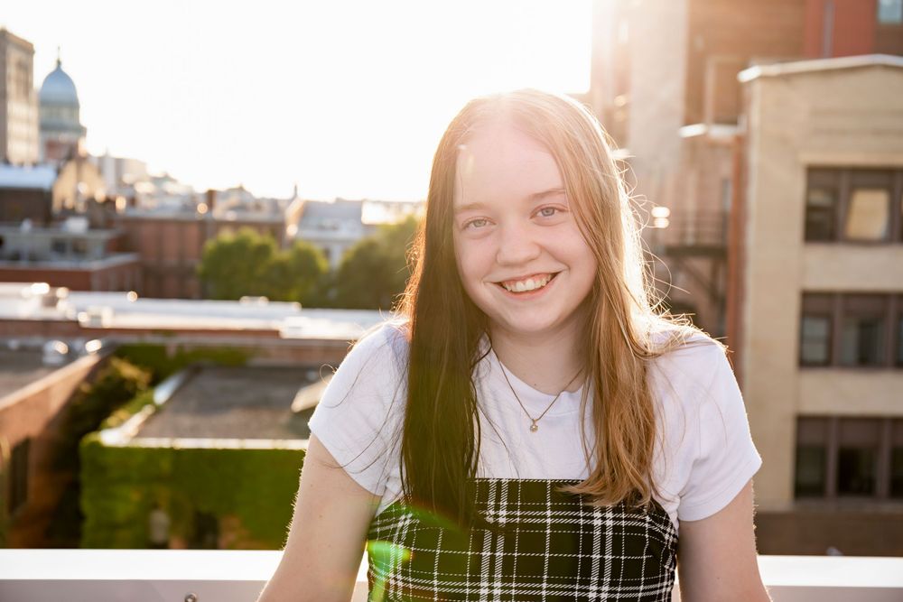 Sunlit rooftop portrait showcasing playful plaid dress outfit in urban setting.
