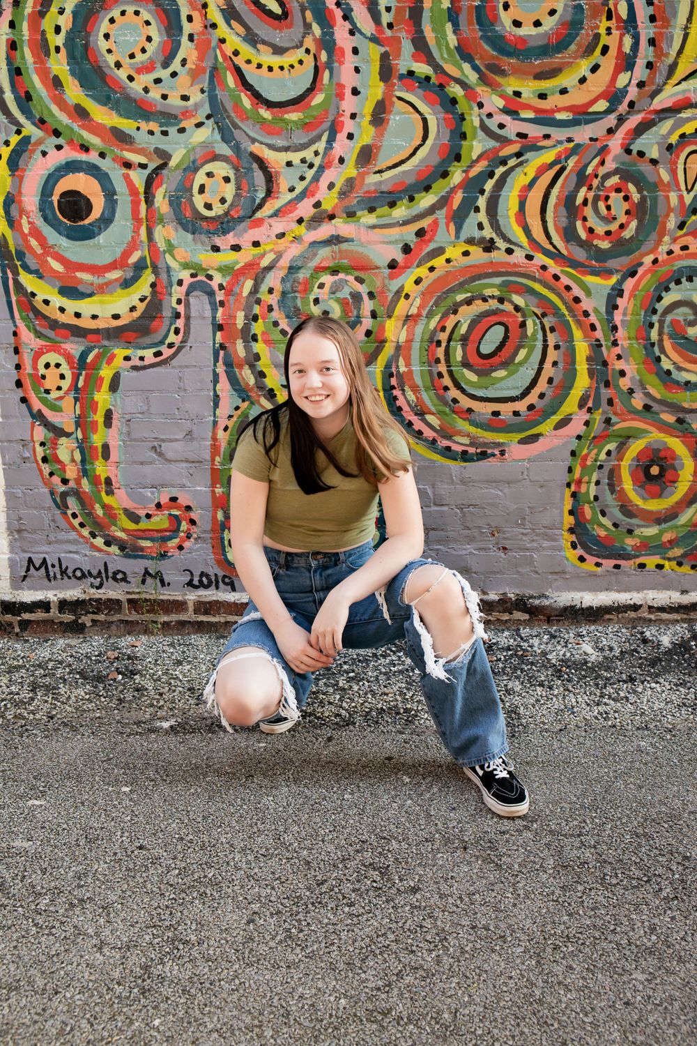 Person crouching in front of colorful circular pattern street art mural.