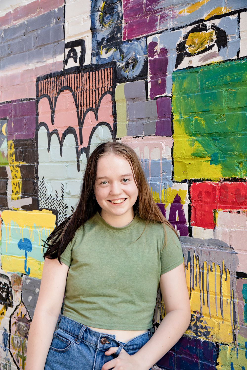 Person in green shirt poses against colorful geometric street art mural.