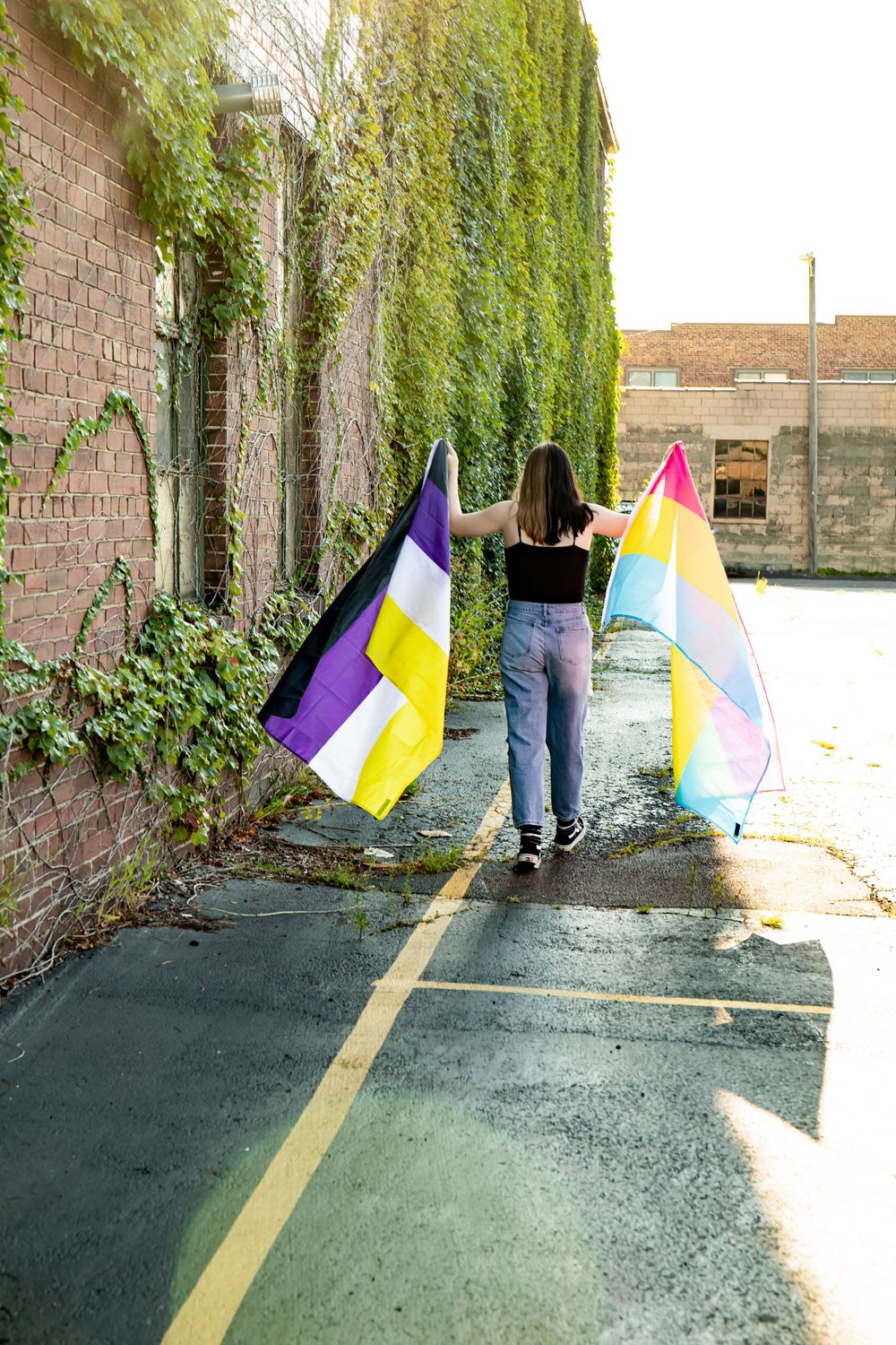Back view of person holding flags while standing on path near ivy-covered wall.