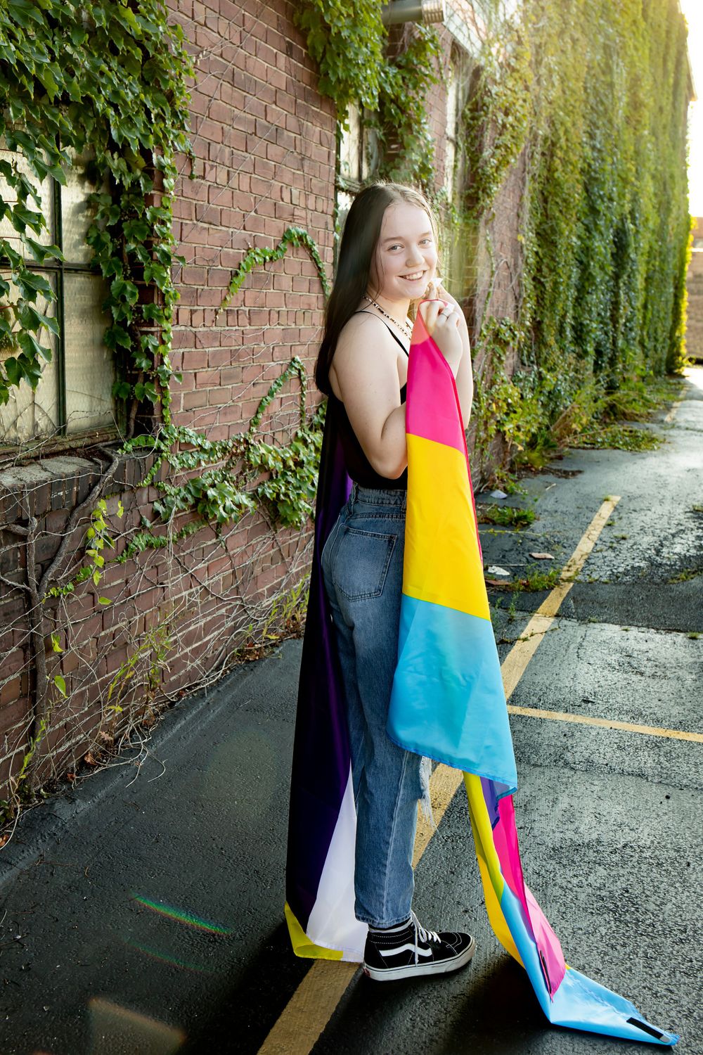 Person holding colorful flag while standing near ivy-covered brick wall.