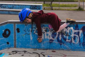 erschöpftes 3jähriges Mädchen mit Samtkleid und Fahrradhelm auf dem Skaterplatz