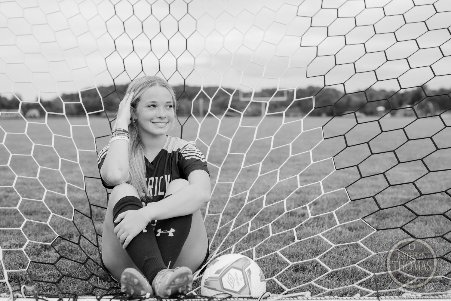 Black and white portrait of athlete sitting in soccer goal net with ball.