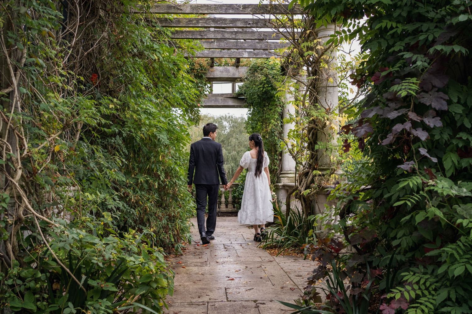 Couple walking down a garden pathway covered in vines and greenery.