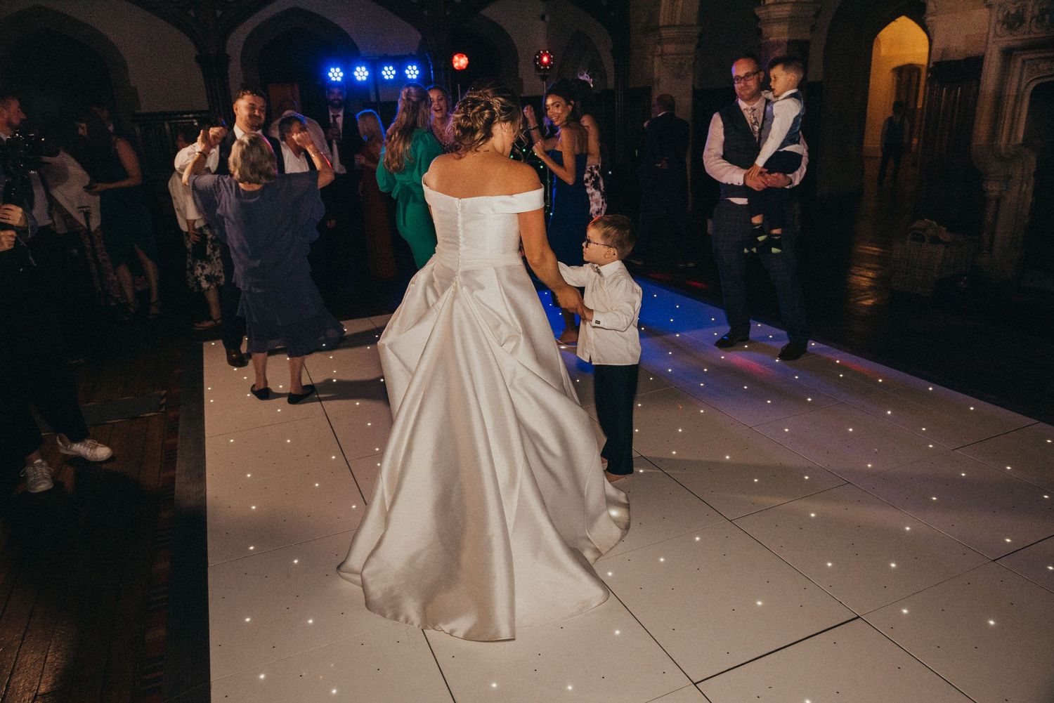 Wedding reception scene with guests watching dancing on a light-up floor.