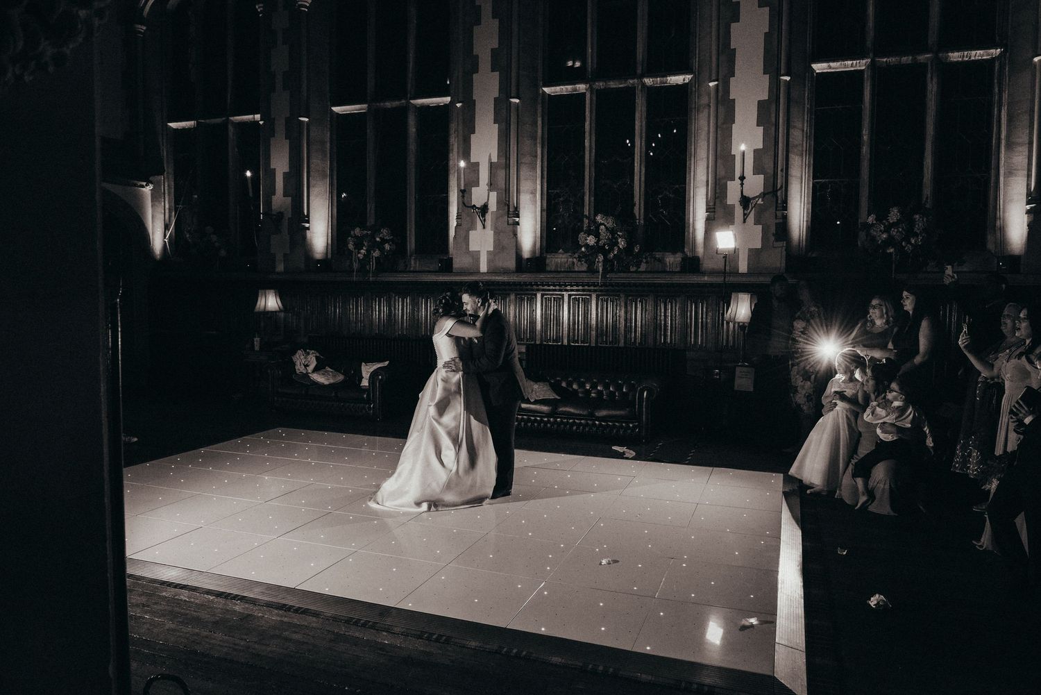 Couple dancing in a dimly lit vintage hall with atmospheric lighting.