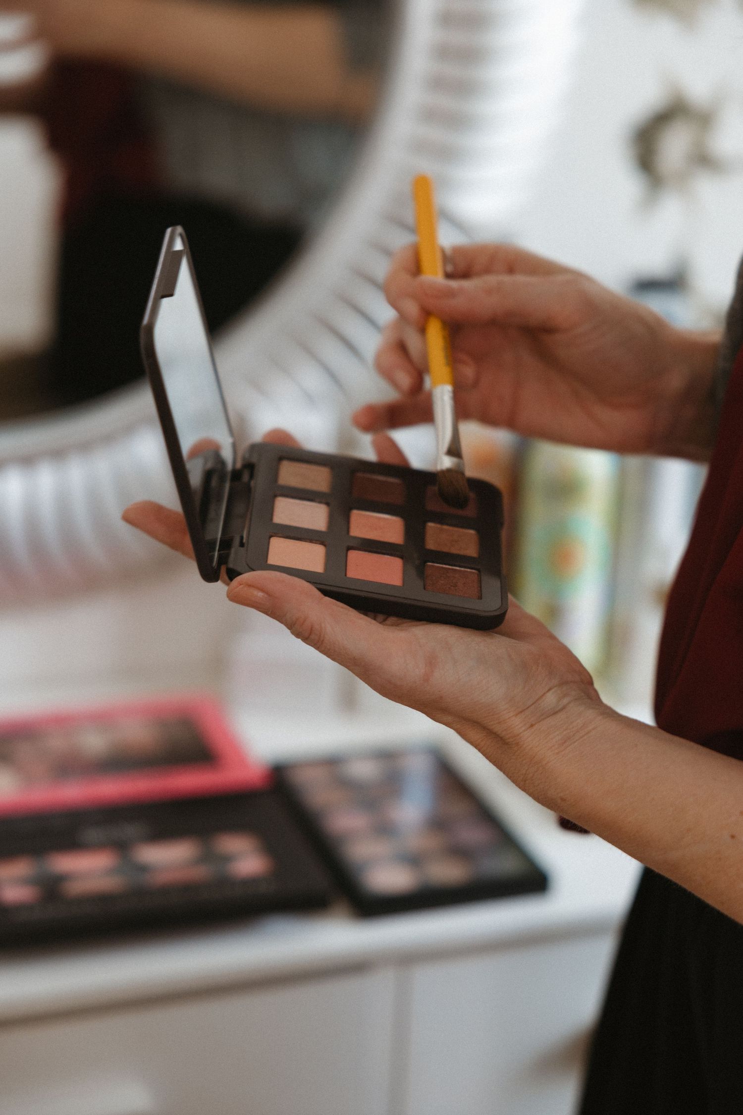 Close-up shot of hands holding and applying makeup with brushes and an eyeshadow palette.
