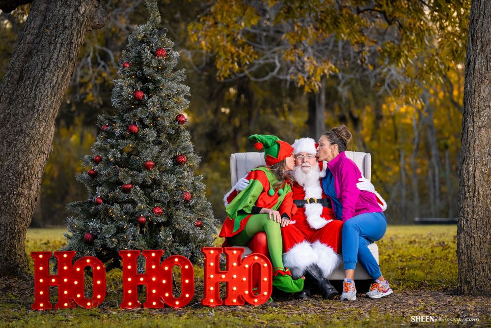 Festive holiday scene with bright costumes against decorated Christmas tree and red light display.