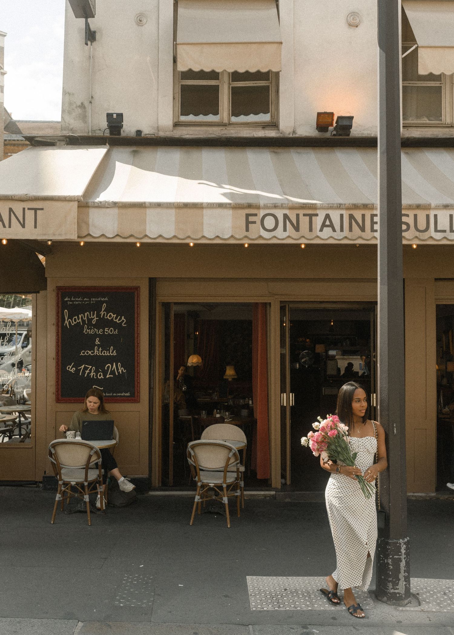 A person in a white dress holds flowers outside Fontaine restaurant in Paris.