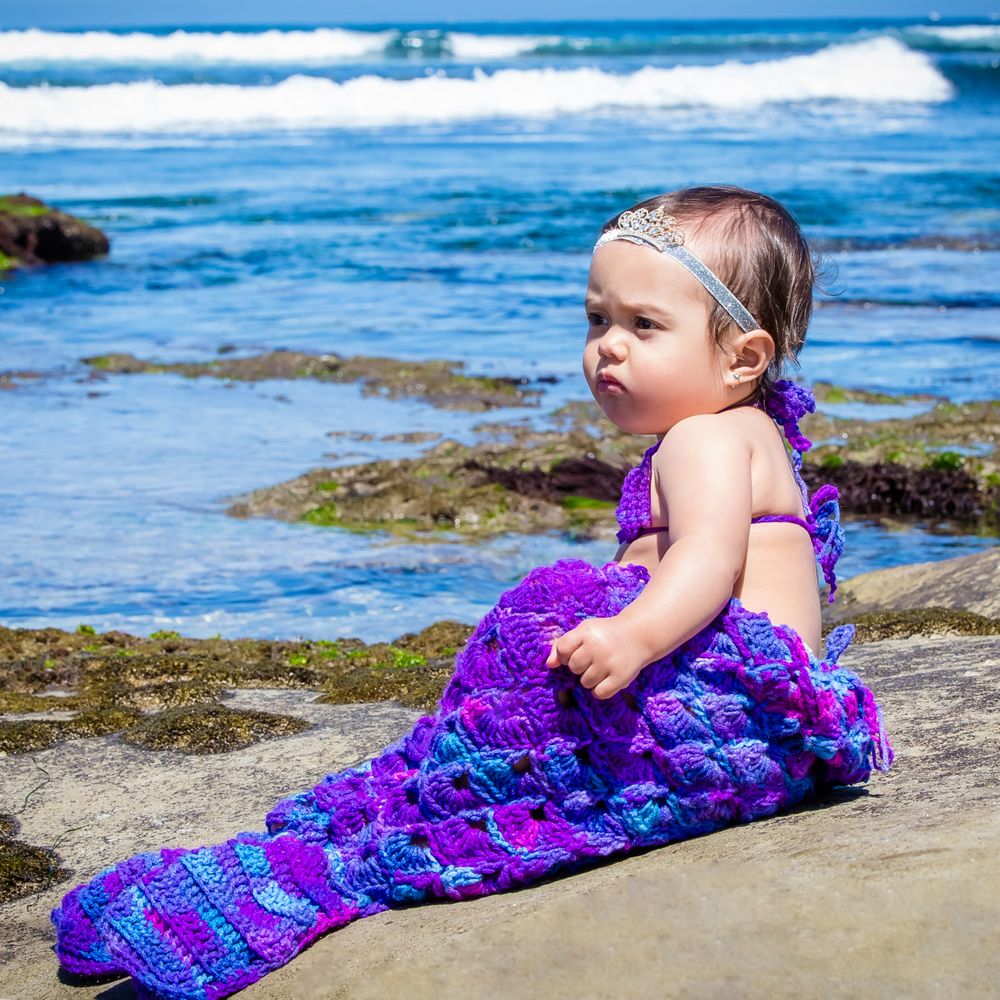 Beachside portrait with waves and rocks featuring a shimmering purple mermaid tail costume.