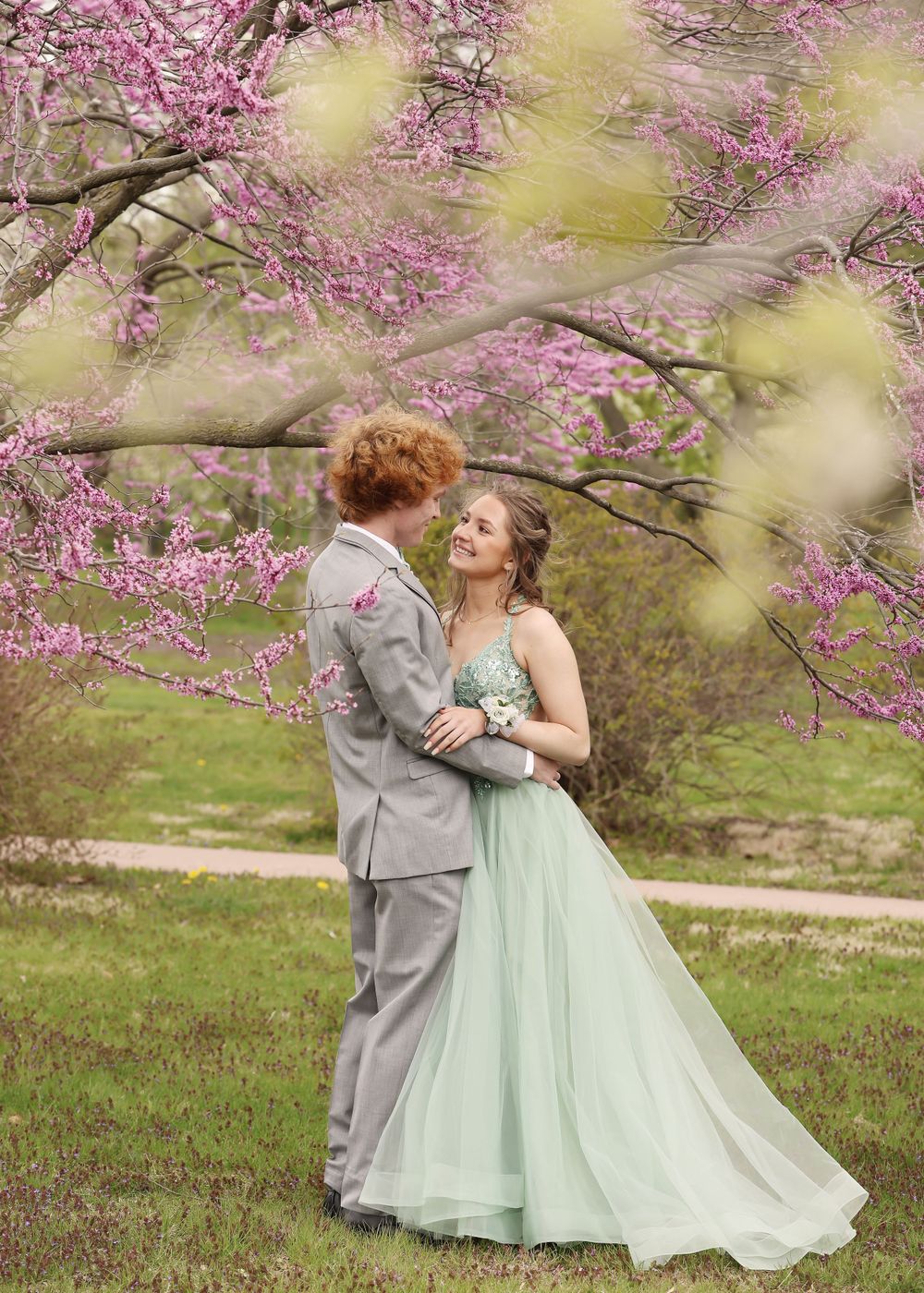 A couple embraces during a spring photoshoot beneath pink flowering trees.