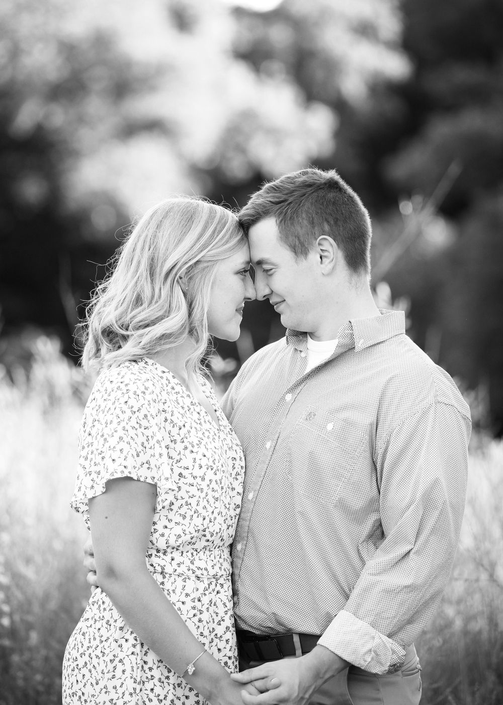 Black and white photo of couple sharing intimate moment in tall grass at sunset.
