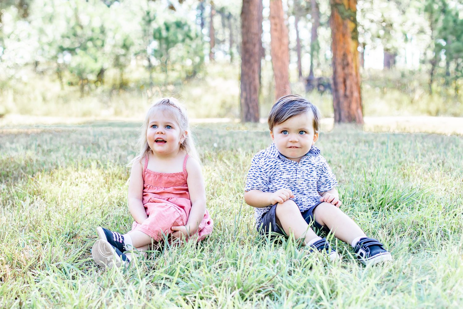 Toddler cousins sit in the grass together in Black Forest, Colorado.