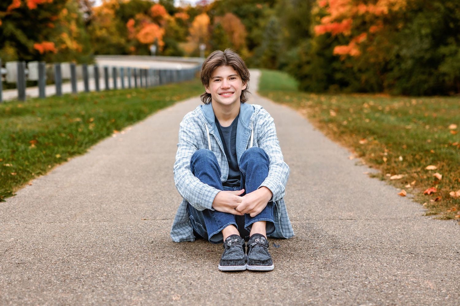 Person sitting cross-legged on path with autumn trees in background.