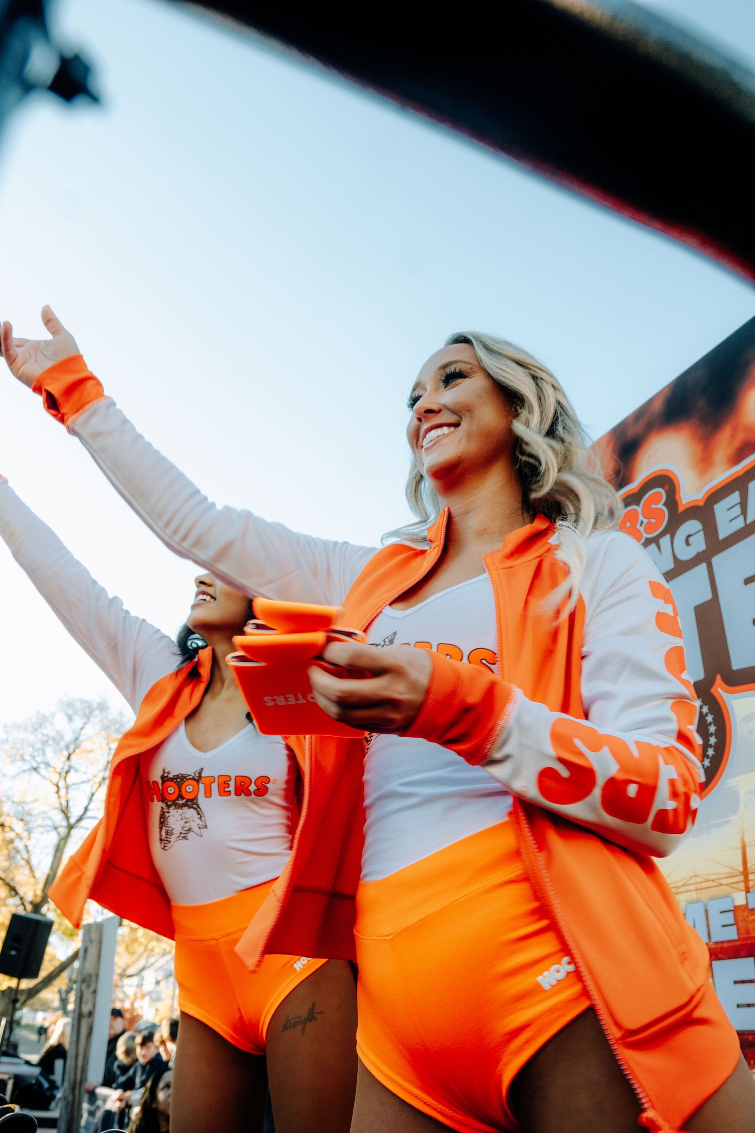 Person in bright orange outfit holding a drink at an outdoor event.