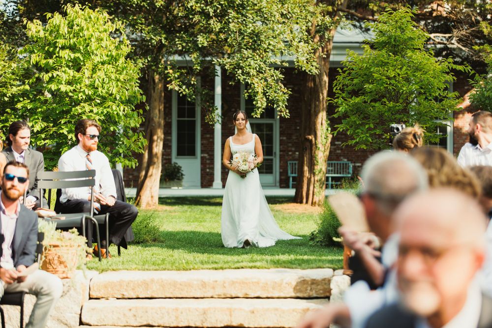 Outdoor wedding ceremony in progress with guests watching under tall trees.