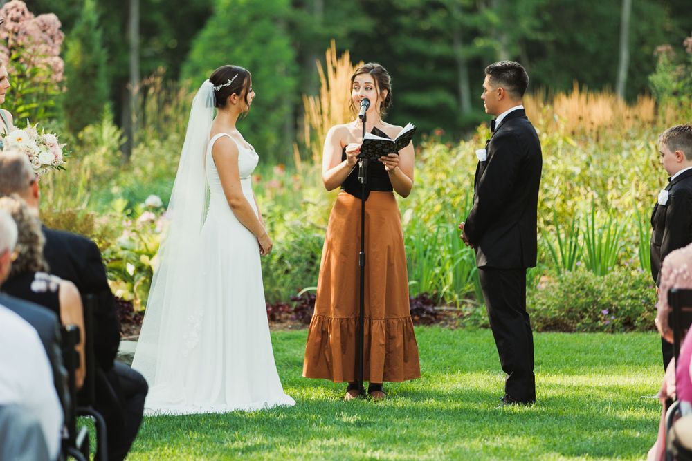 Outdoor garden wedding ceremony with guests seated on white chairs among natural landscaping.