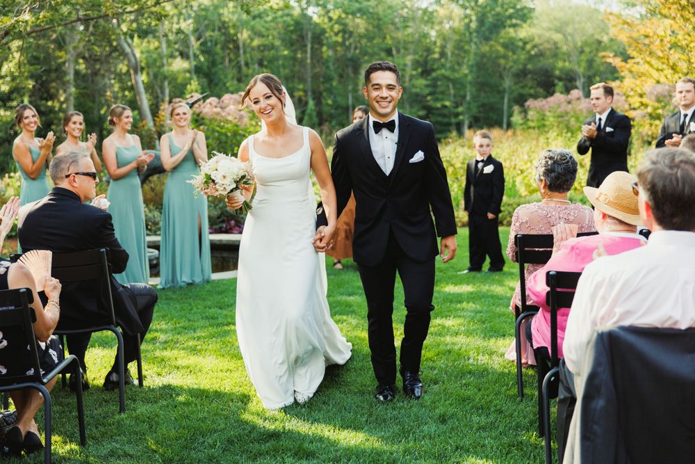 Elegant outdoor wedding ceremony with guests gathered on grass under sunny skies.