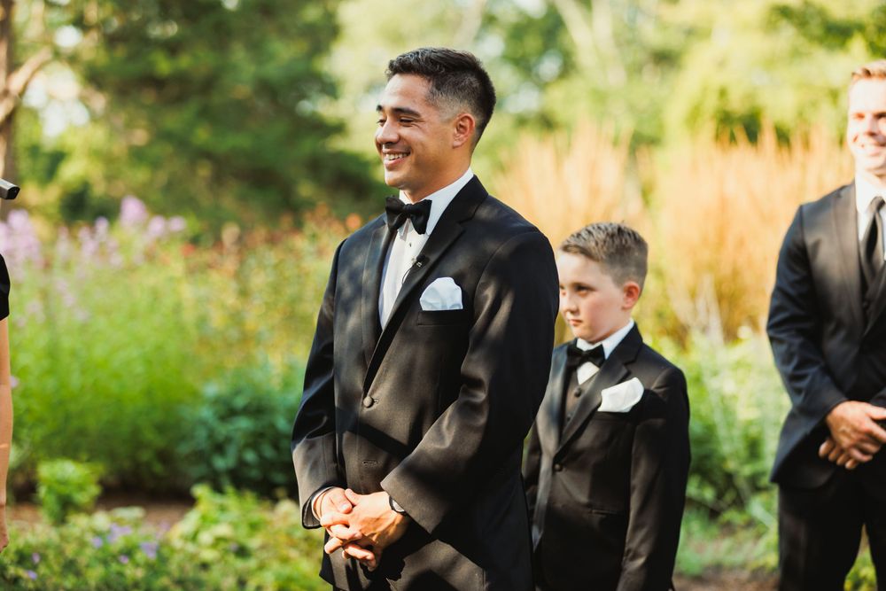 Wedding party members in formal attire standing during outdoor ceremony.