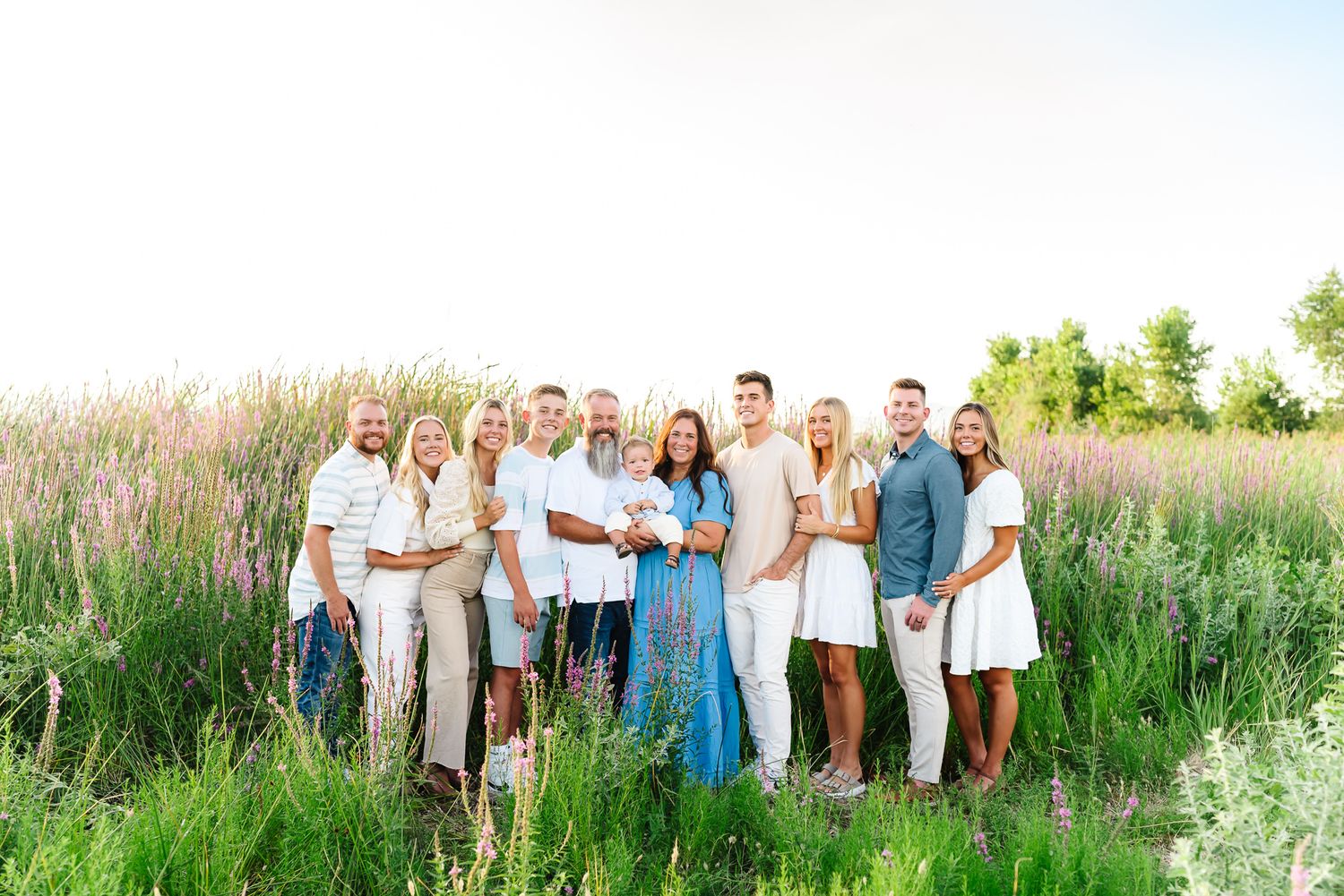 Extended family group photo session in a tall grass field wearing coordinated blue and white outfits.