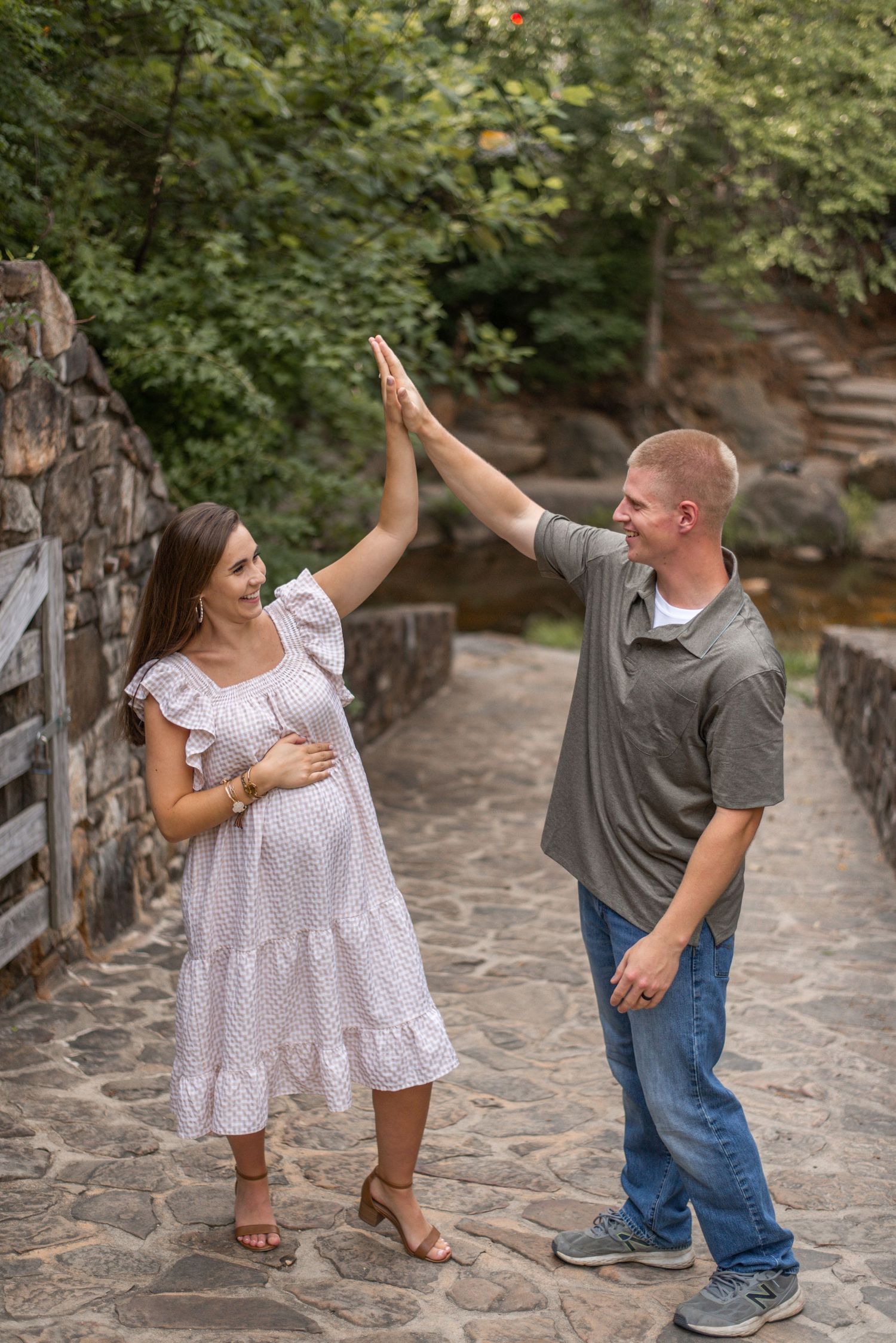 Two people share playful high-fives on a stone pathway surrounded by greenery.
