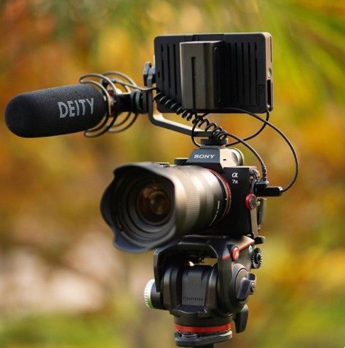 Professional camera setup with Deity microphone and lens mounted on tripod against blurred background.