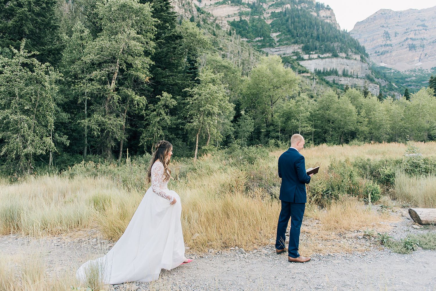 First look wedding moment on a mountain trail surrounded by tall pines and rocky cliffs.