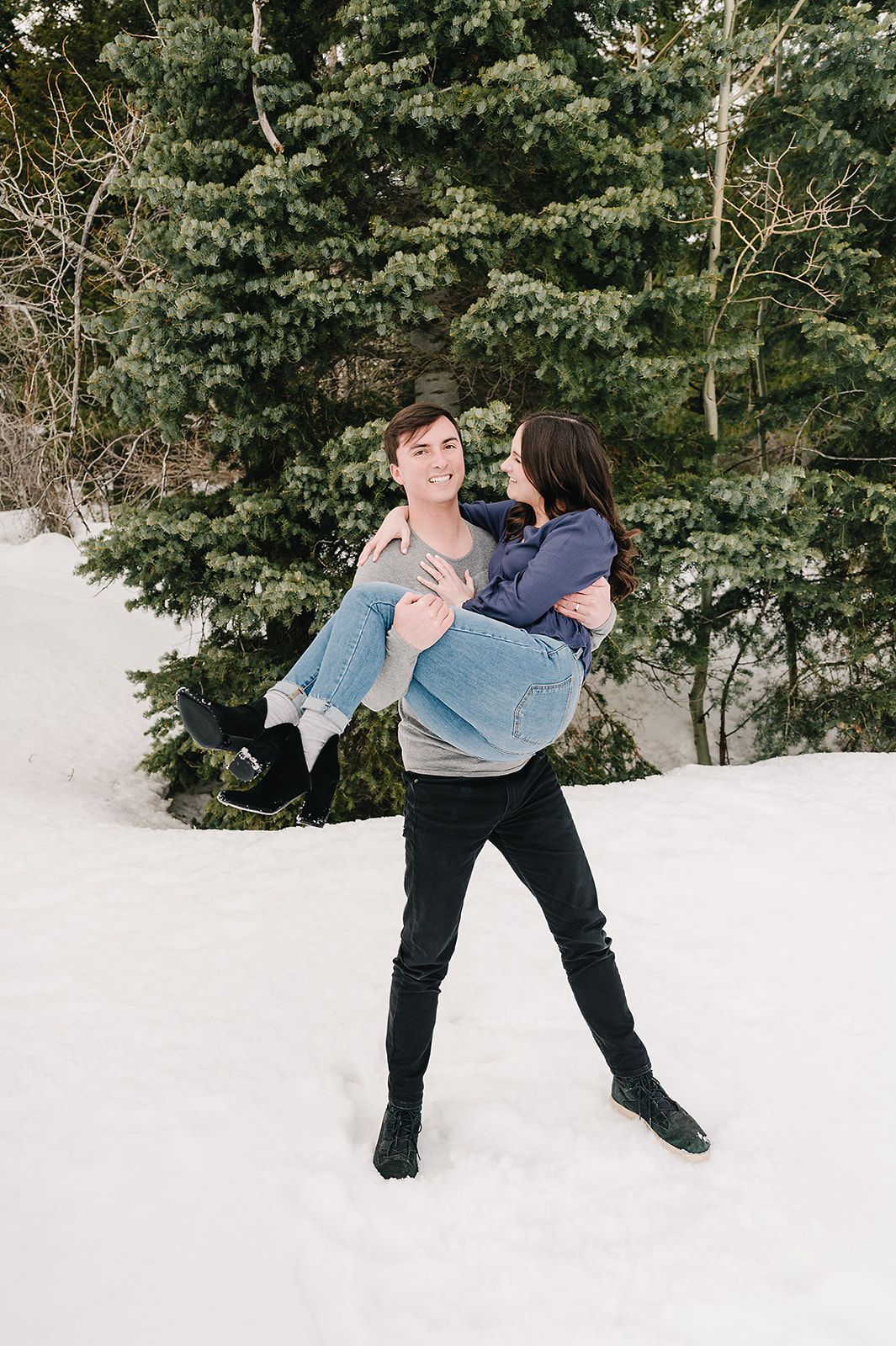 Playful winter engagement photo in snowy forest setting.