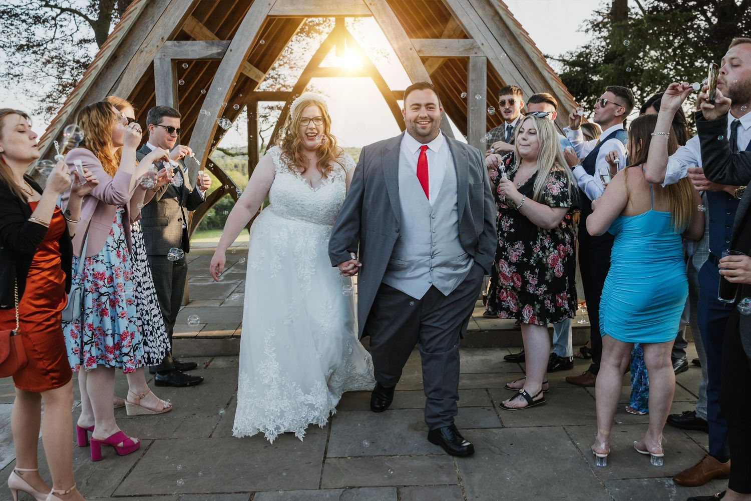Newly wed couple at Highley Manor smiling and walking down a bubble arch of their friends and family smiling at sunset