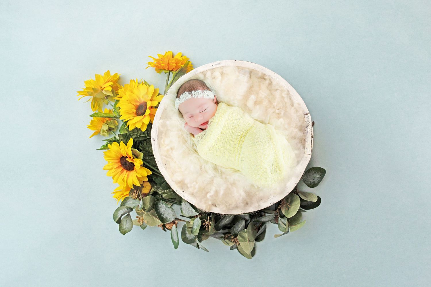 Newborn photography setup with yellow sunflowers and soft cream bedding.