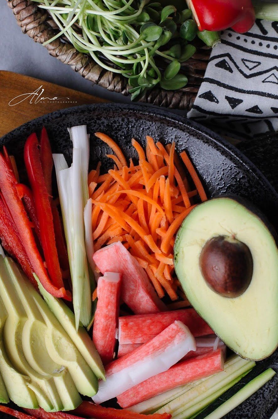 Fresh vegetable platter with sliced avocado, carrots, bell peppers and watermelon on black plate.
