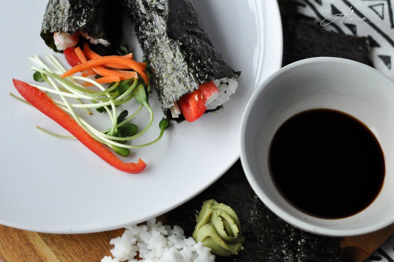 Hand roll sushi with vegetables and soy sauce served with wasabi on geometric patterned placemat.
