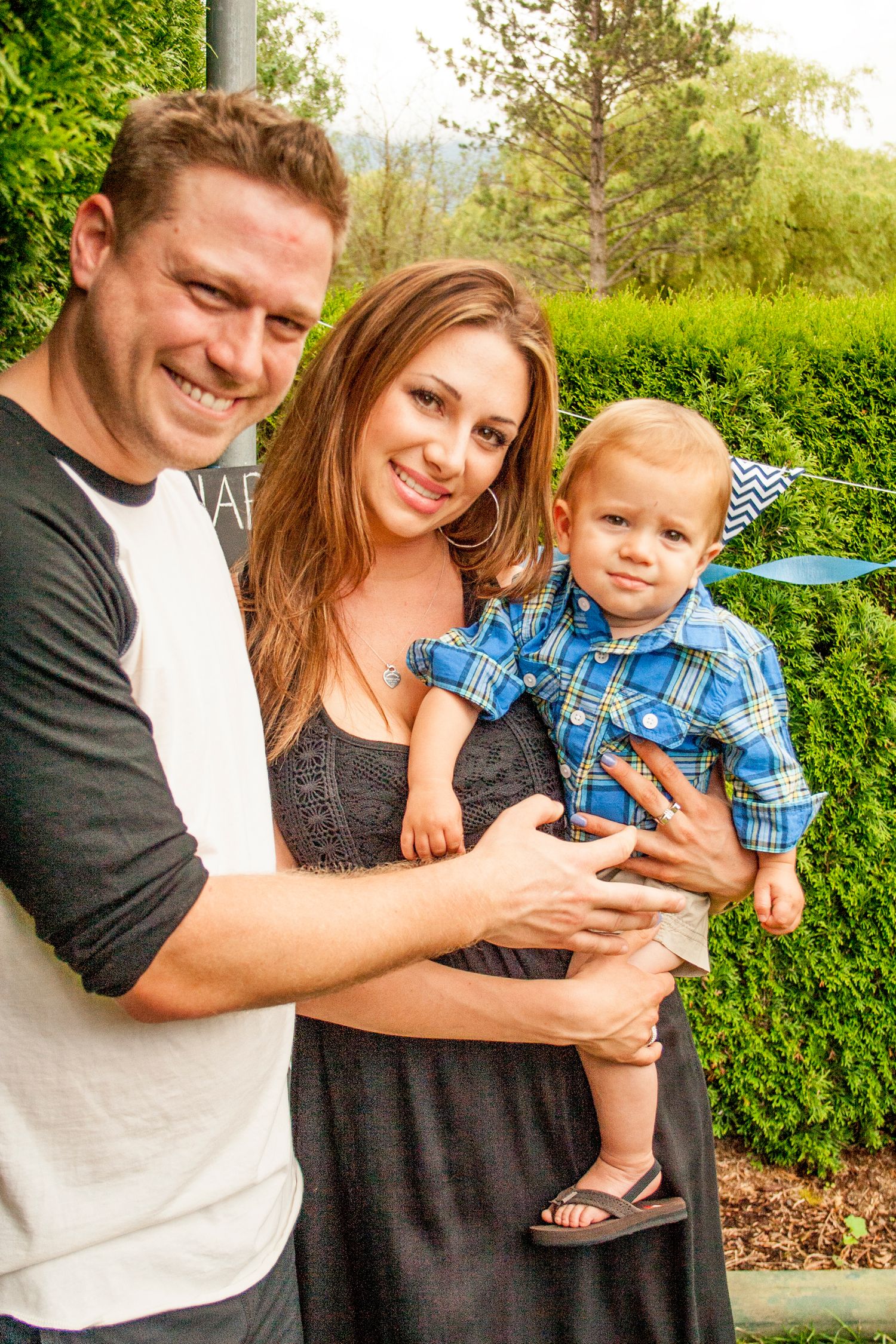 Family pose together in garden setting with greenery backdrop.